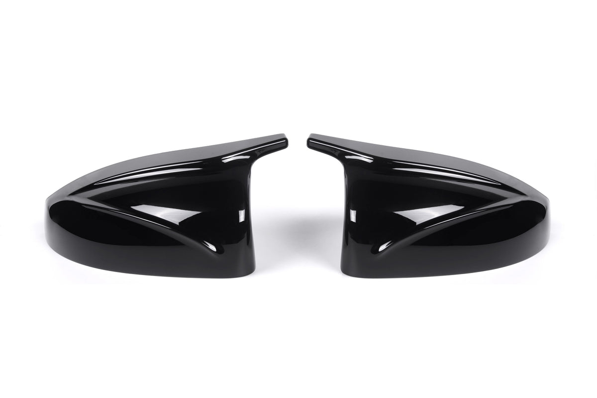 Two sleek black car side mirror covers face each other, reflecting light. They rest on a plain white background, showcasing their glossy finish and aerodynamic design.