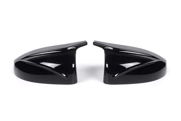 Two sleek black car side mirror covers face each other, reflecting light. They rest on a plain white background, showcasing their glossy finish and aerodynamic design.