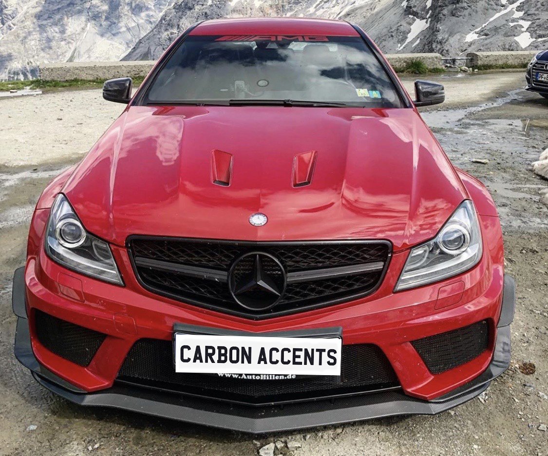 A red Mercedes-Benz car is parked on a mountainous landscape with rocky terrain. The front features "CARBON ACCENTS" and "www.AutoHillen.de" text on the license plate.