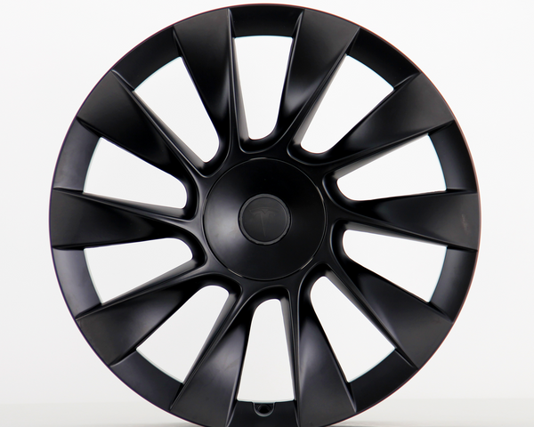 A black, multi-spoke car wheel cover with a subtle central logo sits upright against a plain white background, showcasing its sleek, aerodynamic design.