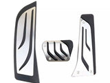 Metal and rubber foot pedals, featuring sleek, curved grooves, are arranged against a plain white background. The set includes an accelerator, brake, and clutch pedal cover, each with distinctive black accents.