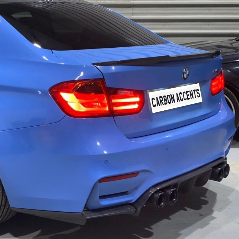 A blue car displays illuminated taillights and a carbon fiber spoiler in a garage setting, with the text "CARBON ACCENTS" on the license plate area.