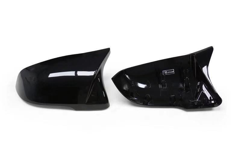 Two shiny black car side mirror covers, one viewed from the top and the other showing the interior with attachment points, rest on a plain white background.