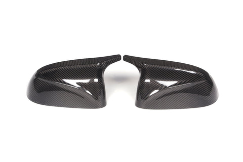 Two carbon fiber car mirror covers are placed side by side, angled inward, on a plain white background. The glossy surface reflects light, highlighting their textured pattern.