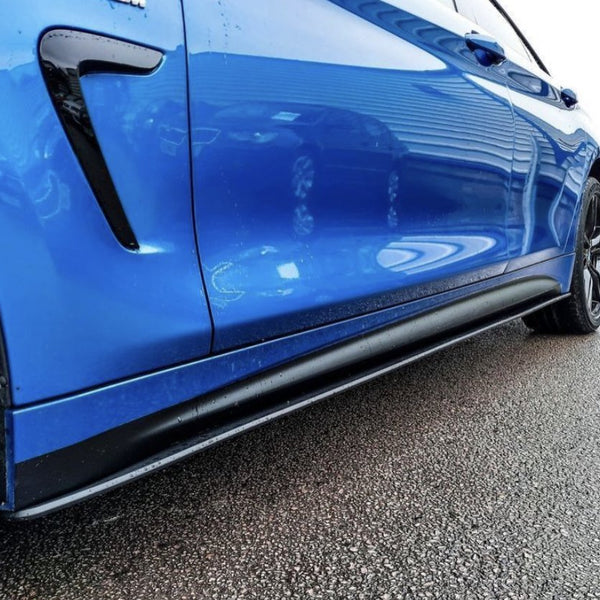 A blue car, parked on a wet asphalt surface, shows its glossy side panel and black wheel, with reflections of nearby structures visible. A sign in the background reads "SEVEN PARKING."