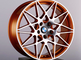 A copper-colored alloy wheel with a complex, multi-spoke design rests on a black pedestal. The BMW logo is in the center. The background is a plain light gray.