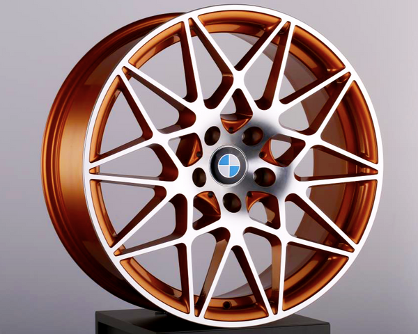 A copper-colored alloy wheel with a complex, multi-spoke design rests on a black pedestal. The BMW logo is in the center. The background is a plain light gray.