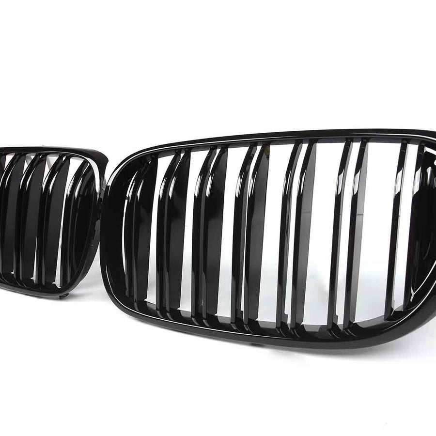 Two sleek, glossy black car grilles are positioned side by side against a plain white background, showcasing vertical slats and slightly curved oval shapes.
