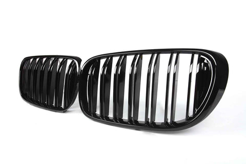 Two sleek, glossy black car grilles are positioned side by side against a plain white background, showcasing vertical slats and slightly curved oval shapes.