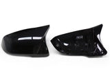 Two glossy black side mirror covers are placed side by side on a plain white background, with the right one showing an interior label.