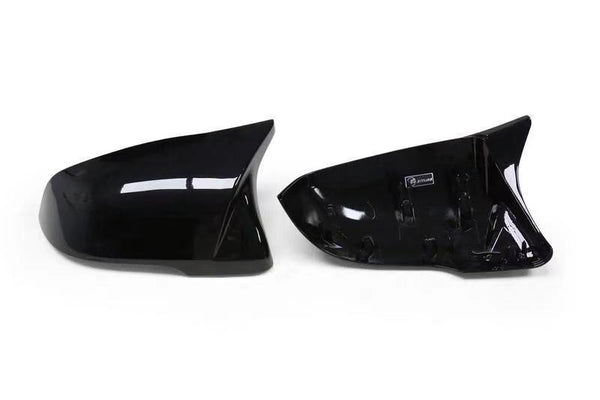 Two glossy black side mirror covers are placed side by side on a plain white background, with the right one showing an interior label.