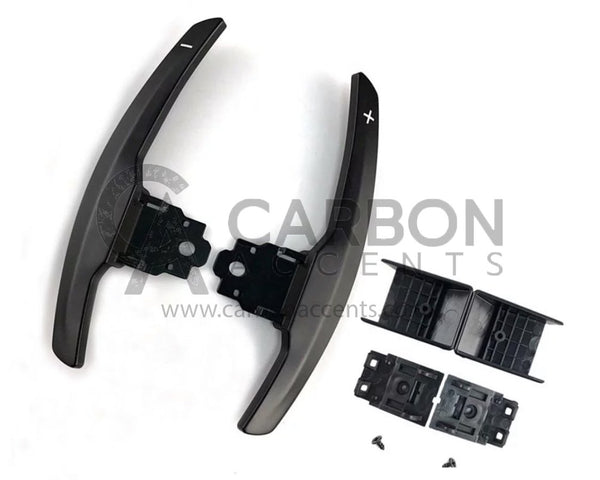 Curved paddle shifters with "+" and "-" symbols, accompanied by brackets and screws, are laid out on a white background. Text: "CARBON ACCENTS www.carbonaccents.com".