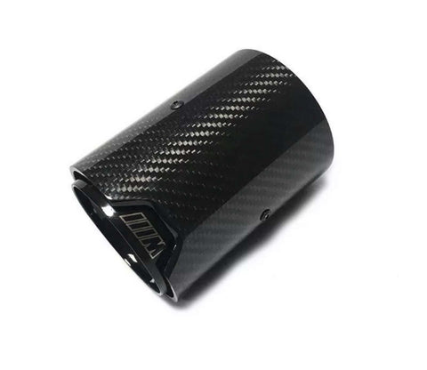 A carbon fiber exhaust tip lies against a plain white background. The surface has a textured pattern. The inner edge features a logo or marking resembling "///M."