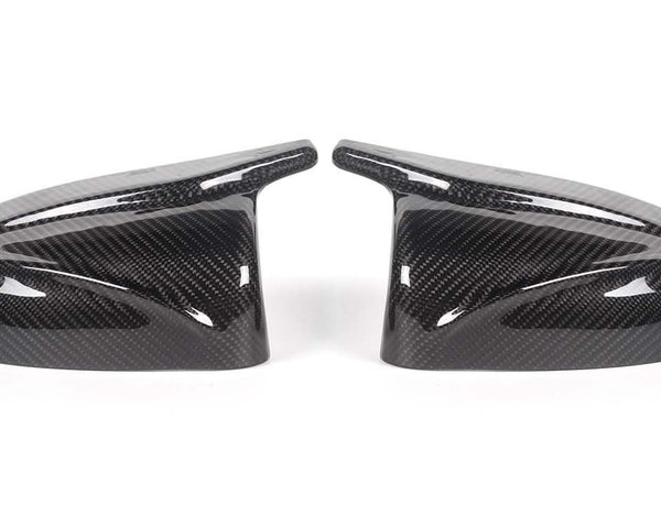 Two carbon fiber side mirror covers rest on a white surface, showcasing a glossy finish and intricate weave pattern, appearing symmetrically aligned.