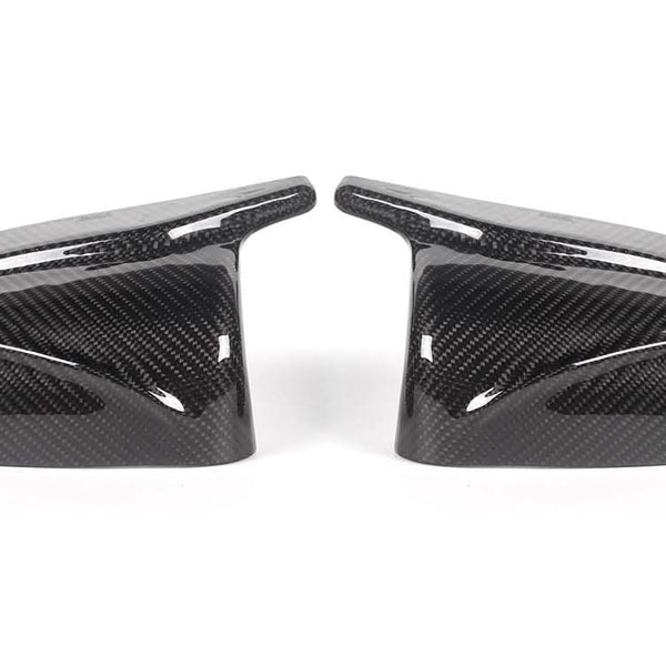 Two carbon fiber side mirror covers rest on a white surface, showcasing a glossy finish and intricate weave pattern, appearing symmetrically aligned.