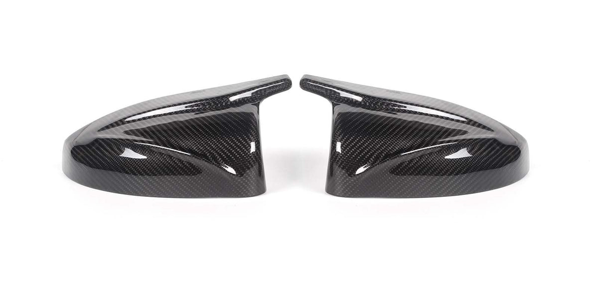 Two carbon fiber side mirror covers rest on a white surface, showcasing a glossy finish and intricate weave pattern, appearing symmetrically aligned.