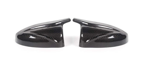 Two carbon fiber side mirror covers rest on a white surface, showcasing a glossy finish and intricate weave pattern, appearing symmetrically aligned.
