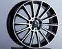 A glossy, black and chrome alloy wheel rests on a pedestal, featuring a three-pointed star emblem at its center, set against a neutral gray background.