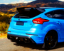 A vibrant blue sports car is parked on a roadside, featuring dual exhausts and a prominent spoiler, with scenic hills and a clear blue sky in the background.