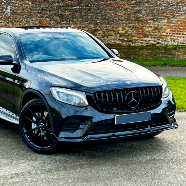 A sleek black SUV with a prominent Mercedes-Benz logo on the grille is parked on a road, set against a backdrop of a brick wall and grass.