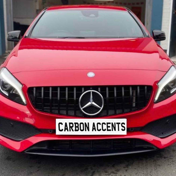 A red car featuring a prominent front grille and sleek headlights is parked outside a garage. The license plate reads "CARBON ACCENTS."