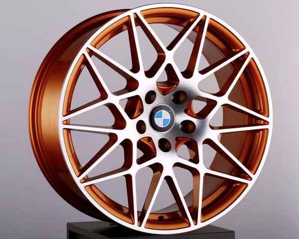 The bronze alloy wheel features an intricate, multi-spoke design, resting on a black pedestal. A blue-and-white circular emblem is at the center, set against a plain background.