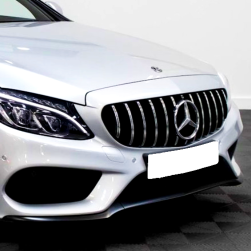 A silver car with a prominent grille and emblem is parked on a patterned floor. The headlights are sleek and angular, highlighting the car's modern design in a well-lit space.