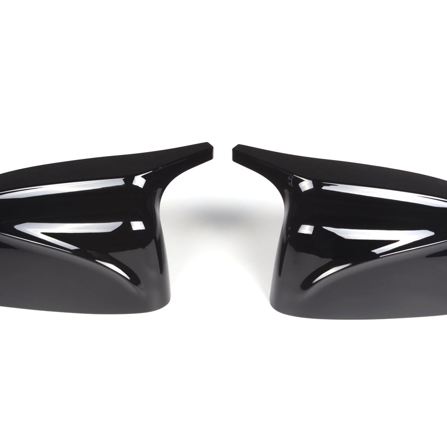 Two glossy black car side mirror covers are positioned symmetrically, facing each other on a plain white background. Their sleek, aerodynamic design reflects light.