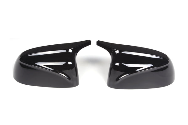 Two glossy black car side mirror covers are positioned symmetrically, facing each other on a plain white background. Their sleek, aerodynamic design reflects light.