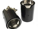 Two black carbon fiber exhaust tips with stainless steel interiors are shown, one upright and the other lying down, showcasing perforated metal inner linings and a logo marked 