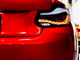 A red car's rear with distinct tail lights is stationary in a well-lit garage, emphasizing its sleek design and reflective surface.