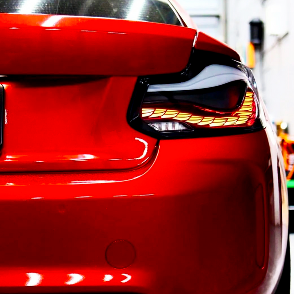A red car's rear with distinct tail lights is stationary in a well-lit garage, emphasizing its sleek design and reflective surface.