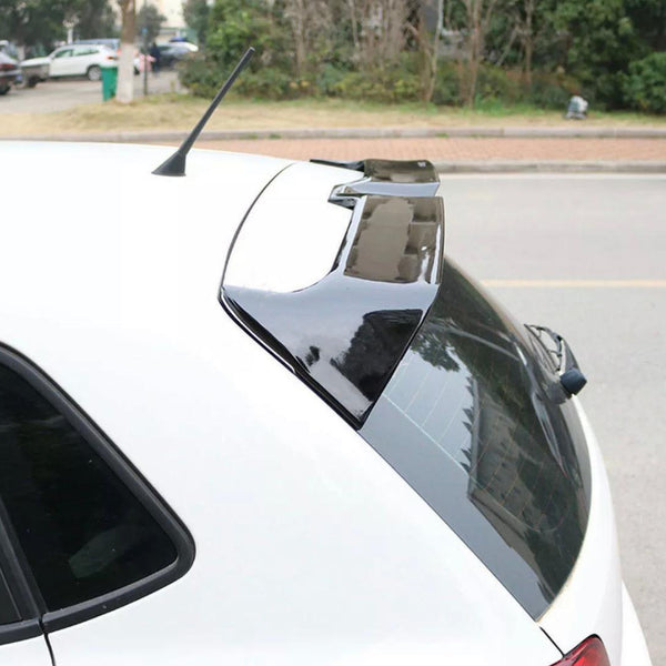 A car with a black rear spoiler is parked on a street. Its antenna is visible on the roof, and trees are in the background, suggesting an urban suburban setting.