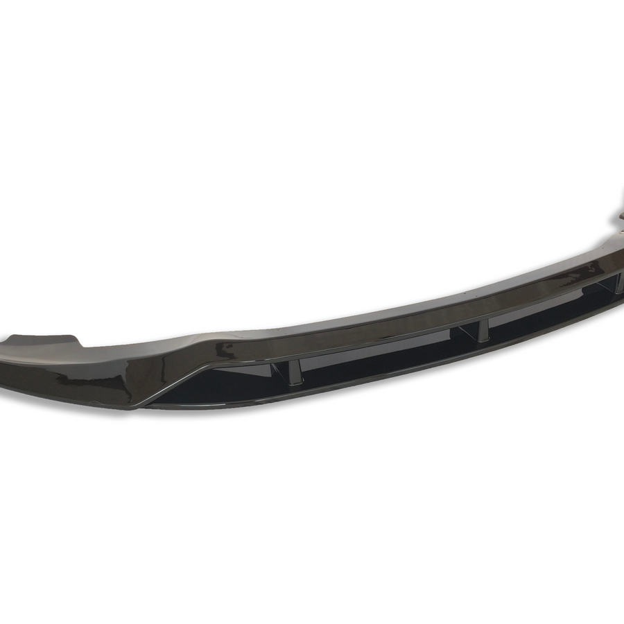 A glossy black car bumper lip sits isolated against a white background, showcasing its curved aerodynamic design and reflective surface.