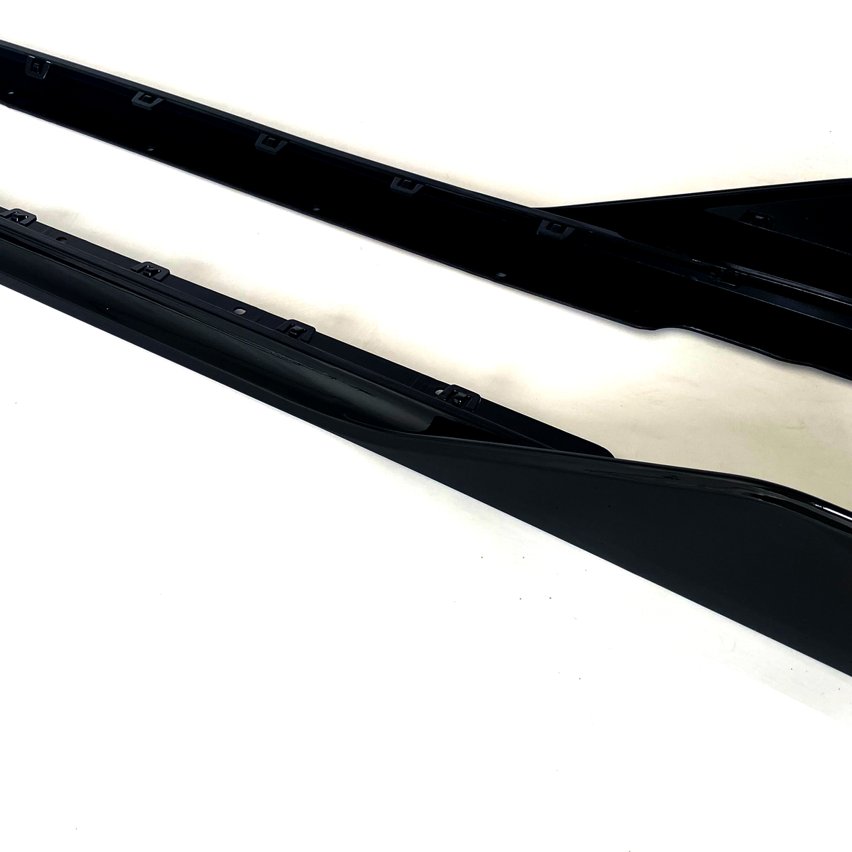 Two black side skirts, sleek and elongated, are positioned parallel on a plain white background.