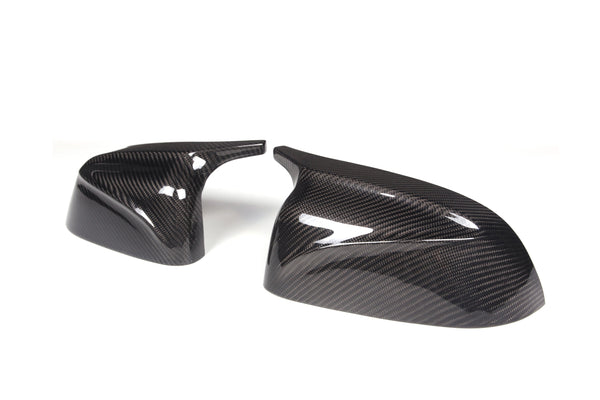 Two glossy carbon fiber car mirror covers lie side by side on a plain white background, showcasing a sleek, modern design with sharp, angular edges.