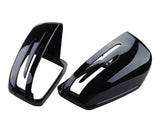 Two glossy black side mirror covers, one upright and one resting, feature elongated vents. They are isolated on a white background, likely automotive parts.