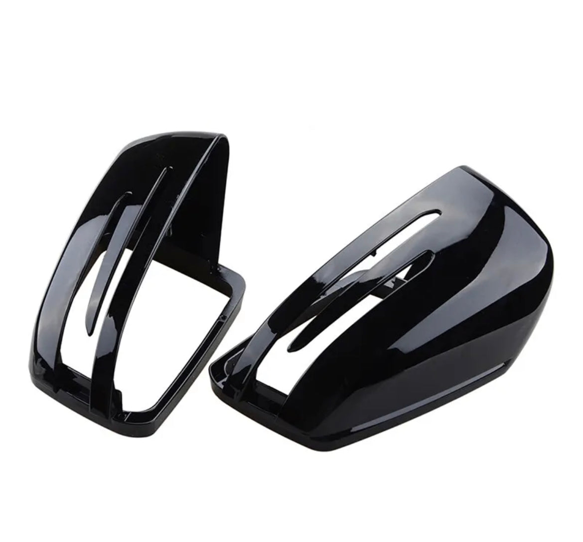 Two glossy black side mirror covers, one upright and one resting, feature elongated vents. They are isolated on a white background, likely automotive parts.