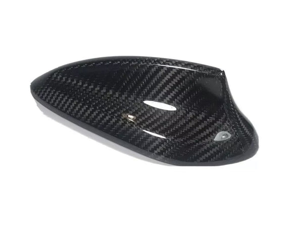 Carbon fiber car side mirror cover, sleek and glossy, lies on a white background, showcasing its weave pattern and aerodynamic shape.