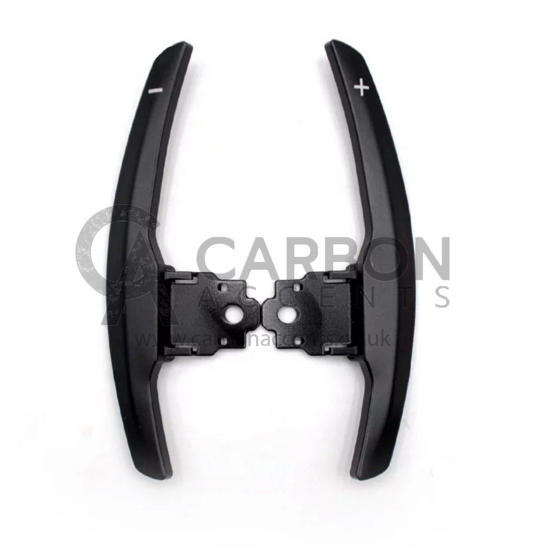 Paddle shifters with plus and minus symbols attached to a black base, used for car gear shifting. Background is plain white with faint text reading "CARBON" and "www.carbonac.uk".
