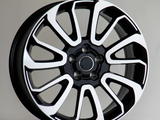 A black and white alloy wheel with ten curved spokes sits against a plain, light-gray background, resting on a flat surface.