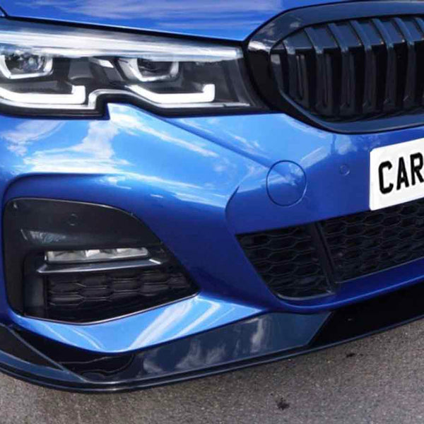 A blue car with a front view displaying sleek headlights and a prominent grille. It is parked on a pavement. The license plate reads "CARBON ACCENTS."