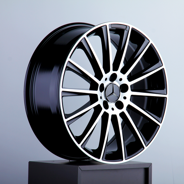 A sleek, black alloy wheel with a silver rim and star emblem rests on a pedestal against a plain grey background.