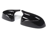 Glossy black car mirror covers resting on a plain white background, displaying sleek, aerodynamic curves and smooth surfaces.