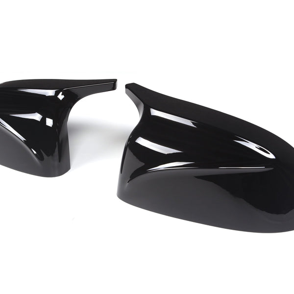 Glossy black car mirror covers resting on a plain white background, displaying sleek, aerodynamic curves and smooth surfaces.