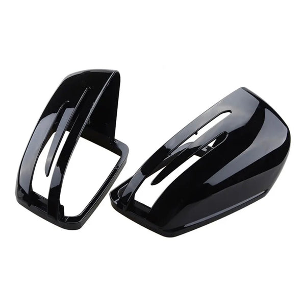 Two glossy black car mirror covers lie on a plain white surface. One is positioned upright, while the other is tilted, displaying their aerodynamic design and sleek finish.