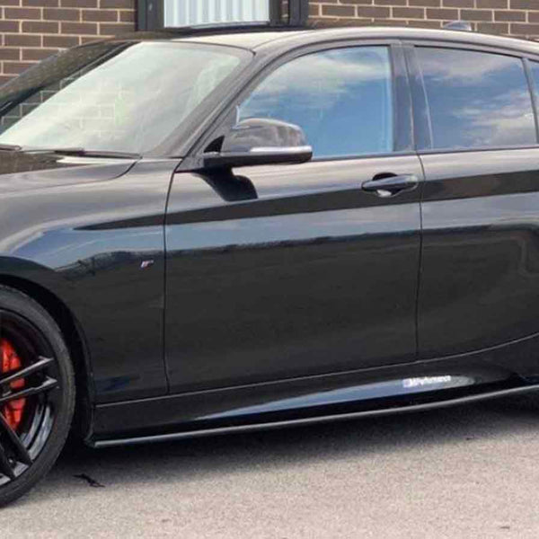 A shiny black car, parked on a street, displays red brake calipers and black alloy wheels. It is beside a brick building with large windows.