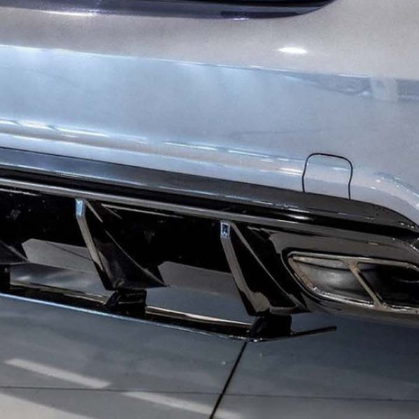 A car's rear bumper features dual exhausts and a black diffuser. The scene is indoors, with the vehicle parked on a glossy tiled floor.