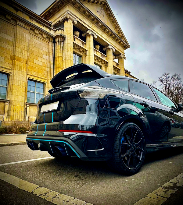 A sleek black car parked on a street in front of a neoclassical building with tall columns and a pediment. Sky is overcast, adding to the dramatic atmosphere.