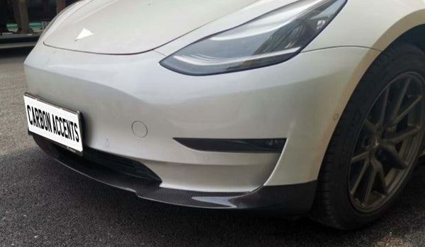 A white car with carbon fiber accents is parked on an asphalt surface. The license plate reads "CARBON ACCENTS."
